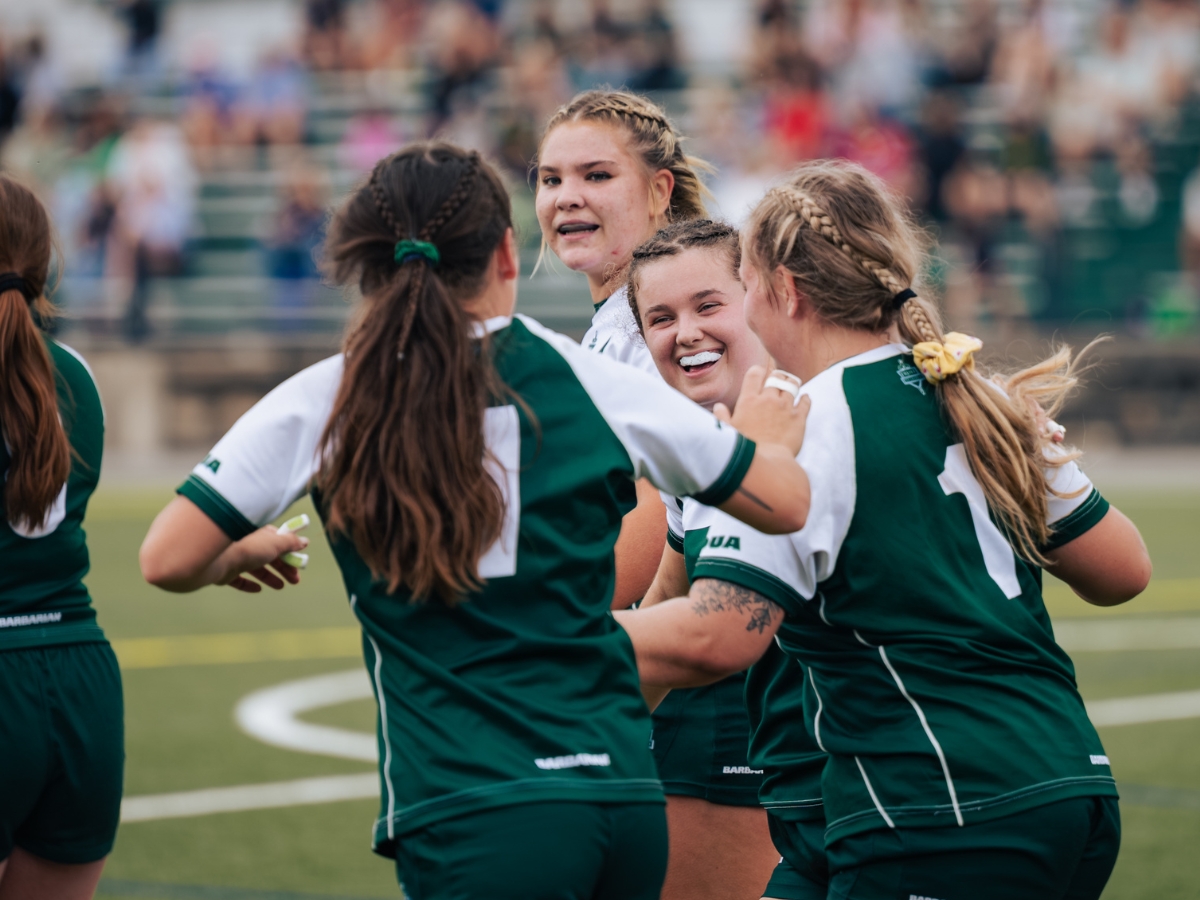 A group of women's rugby players on the field, smiling at each other