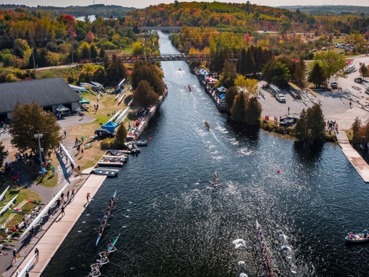 An aerial shot of a river, with boats rowing down it, trees changing in the background