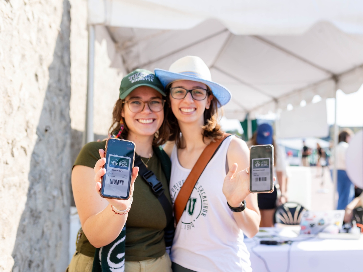 Two people smiling, holding up their phone showing the Trent Alumni Perks App