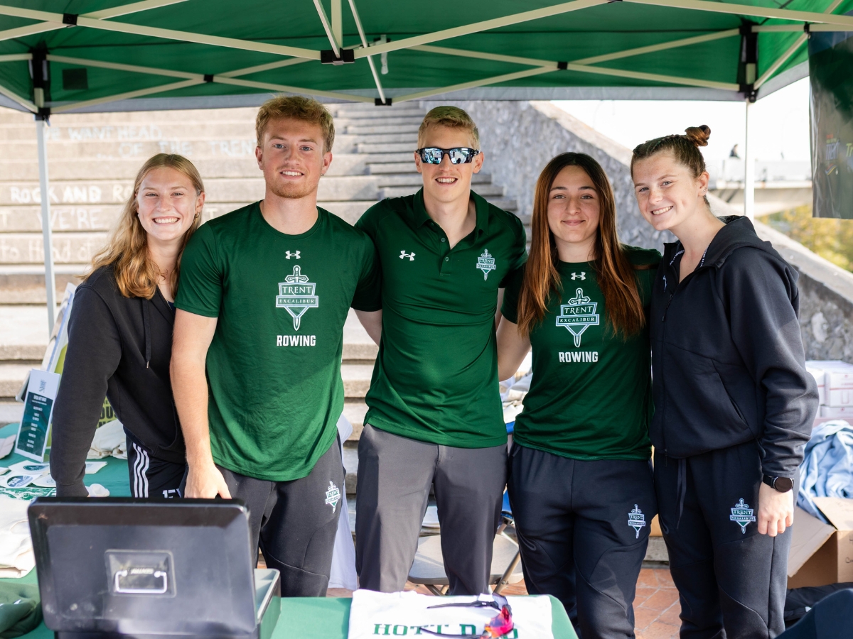 A group of people standing outside under a tent, smiling at the camera
