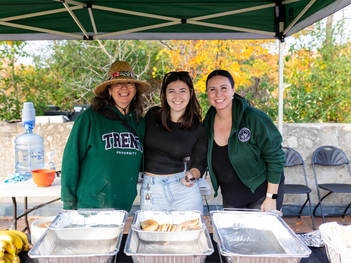 Three people smiling at the camera, showing off a tray of pancakes in front of them