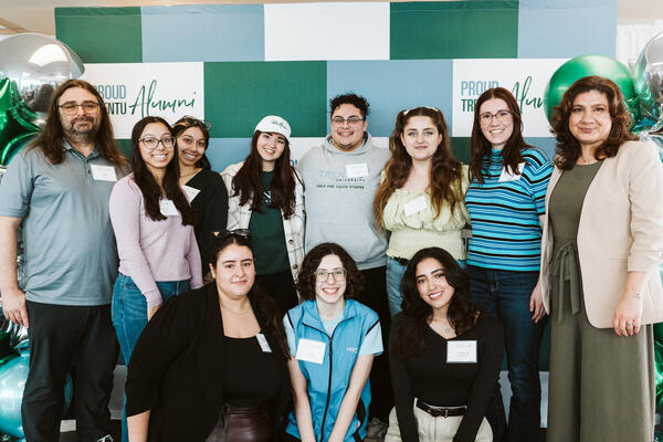 Group photo of Trent Durham alumni with professor in front of backdrop.