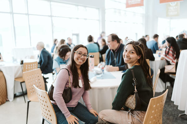 2 women sitting at a table, smiling at the camera
