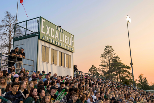 People in the stands of a outdoor game with an Excalibur sign and sunset in the background