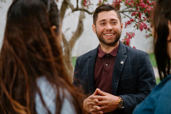 Male in suit jacket speaking with, shot is over the shoulder of 2 women