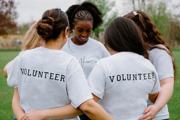 Group of women standing in circle with arms around each other, back of shirts read "Volunteer"