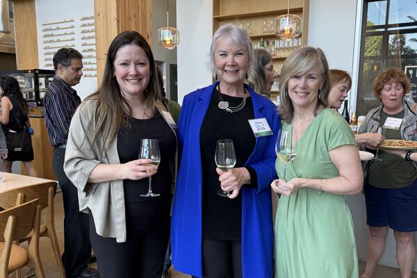 3 women at event smiling at the camera holding wine glasses