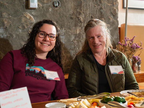 Two people, sitting at a table, smiling at the camera.
