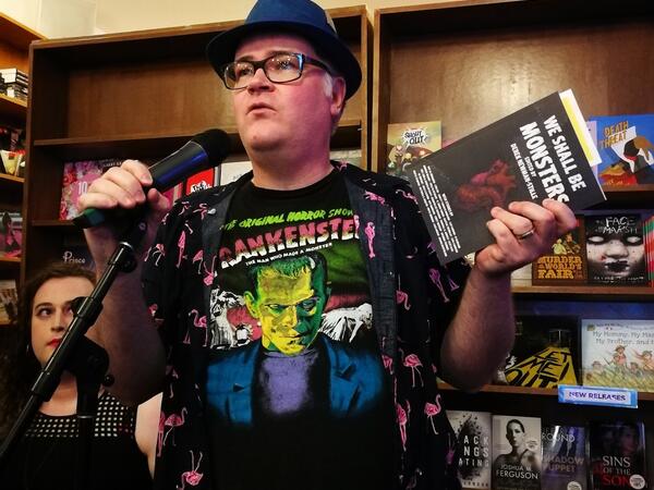 Person holding a book, speaking into a microphone at a book launch