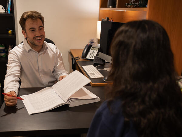 Man in dress shirt meeting with student, book open on table