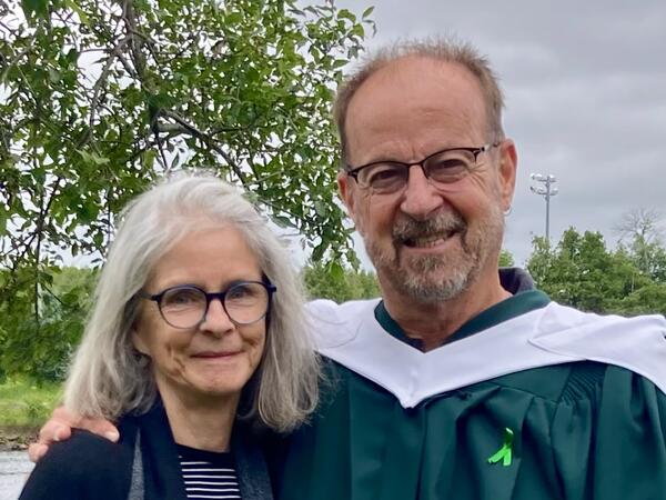 Two people smiling, one wearing graduation regalia