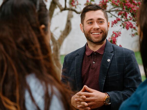 Male in suit jacket speaking with, shot is over the shoulder of 2 women