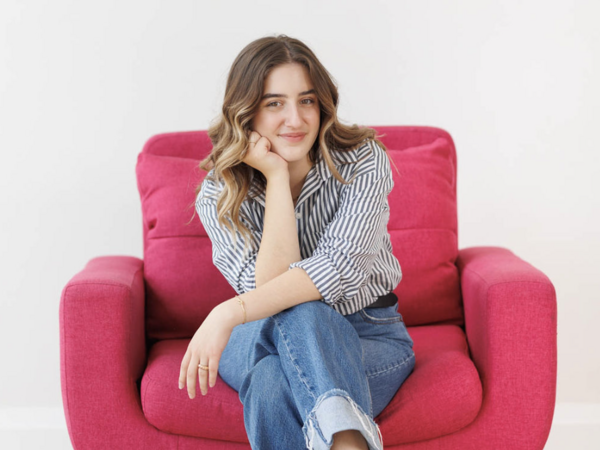 Women sitting on pink chair, legs crossed, smiling