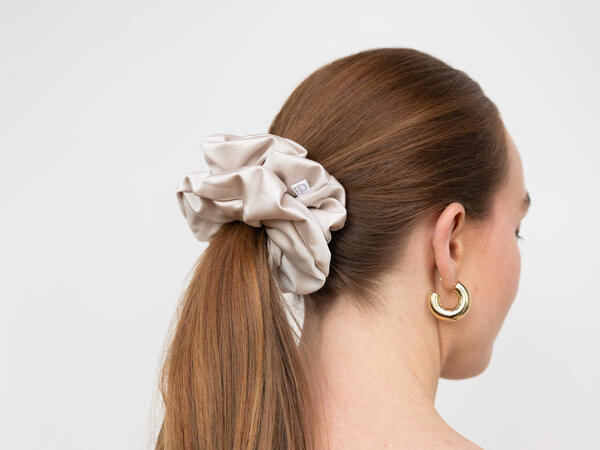 The back of a woman's head with her hair tied up in a ponytail with a satin scrunchie