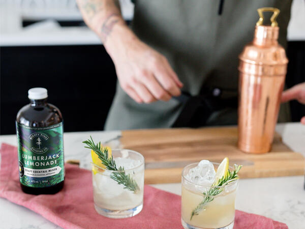 Two cocktail glasses with a mixer and bartender in the background