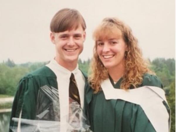 A couple smiling in convocation gowns holding flowers