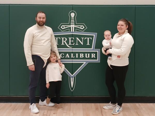 A family of four standing in front of Trent Excalibur logo in a gym
