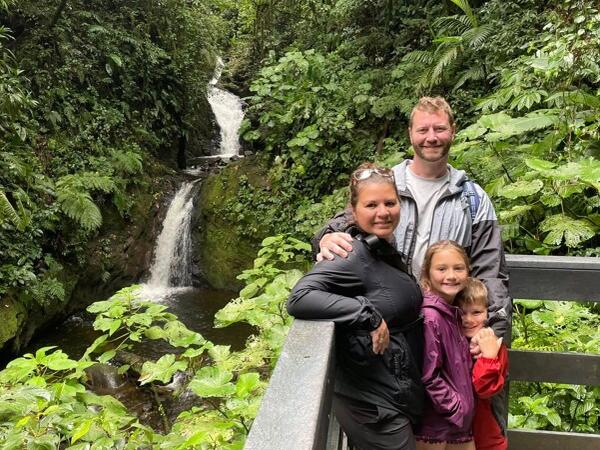 A family of four standing outside with a waterfall behind them