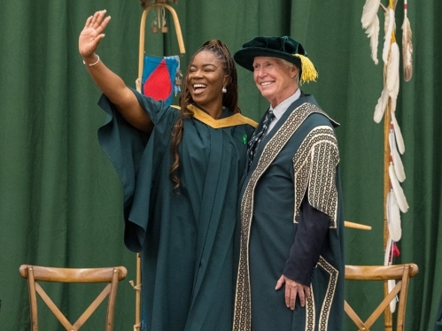 A graduate waves to Convocation crowd next to Chancellor Stephen Stohn