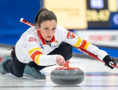 A woman sliding down the ice throwing a curling rock