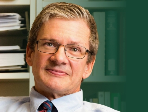 A man with glasses smiling at the camera, with books behind him