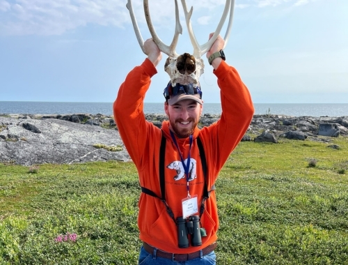 Man standing outside holding a pair of antlers above his head