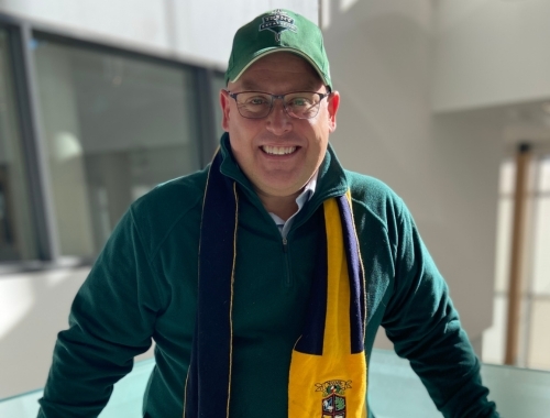 A man with a green hat and Otonabee College scarf on smiling at the camera