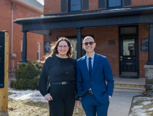 Two people standing outside of a red brick house, smiling at the camera
