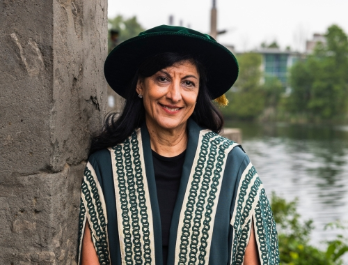 A woman wearing academic regalia, standing outside, smiling at the camera