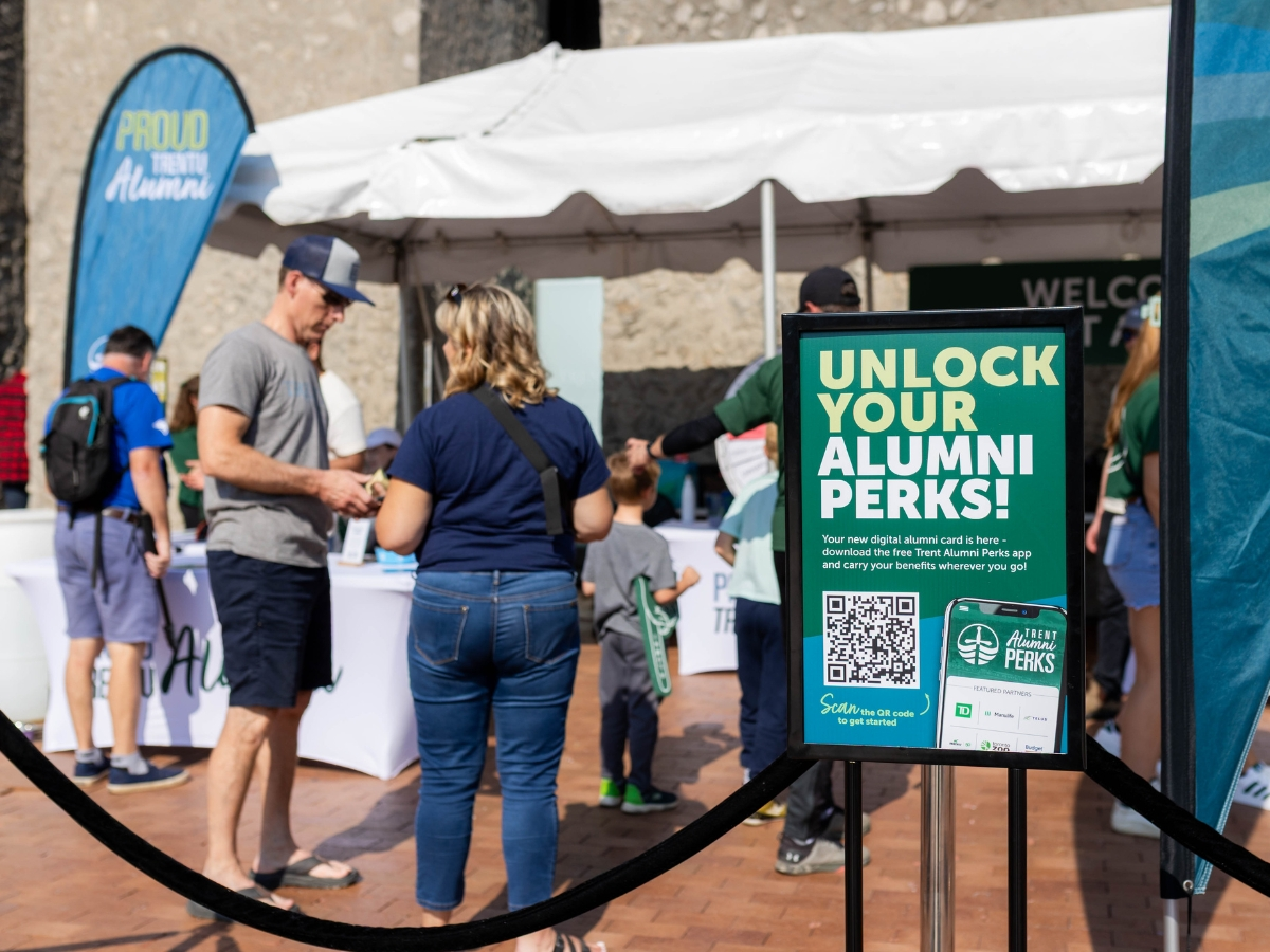 People standing in line outside at a test, with some signage about Alumni Perks