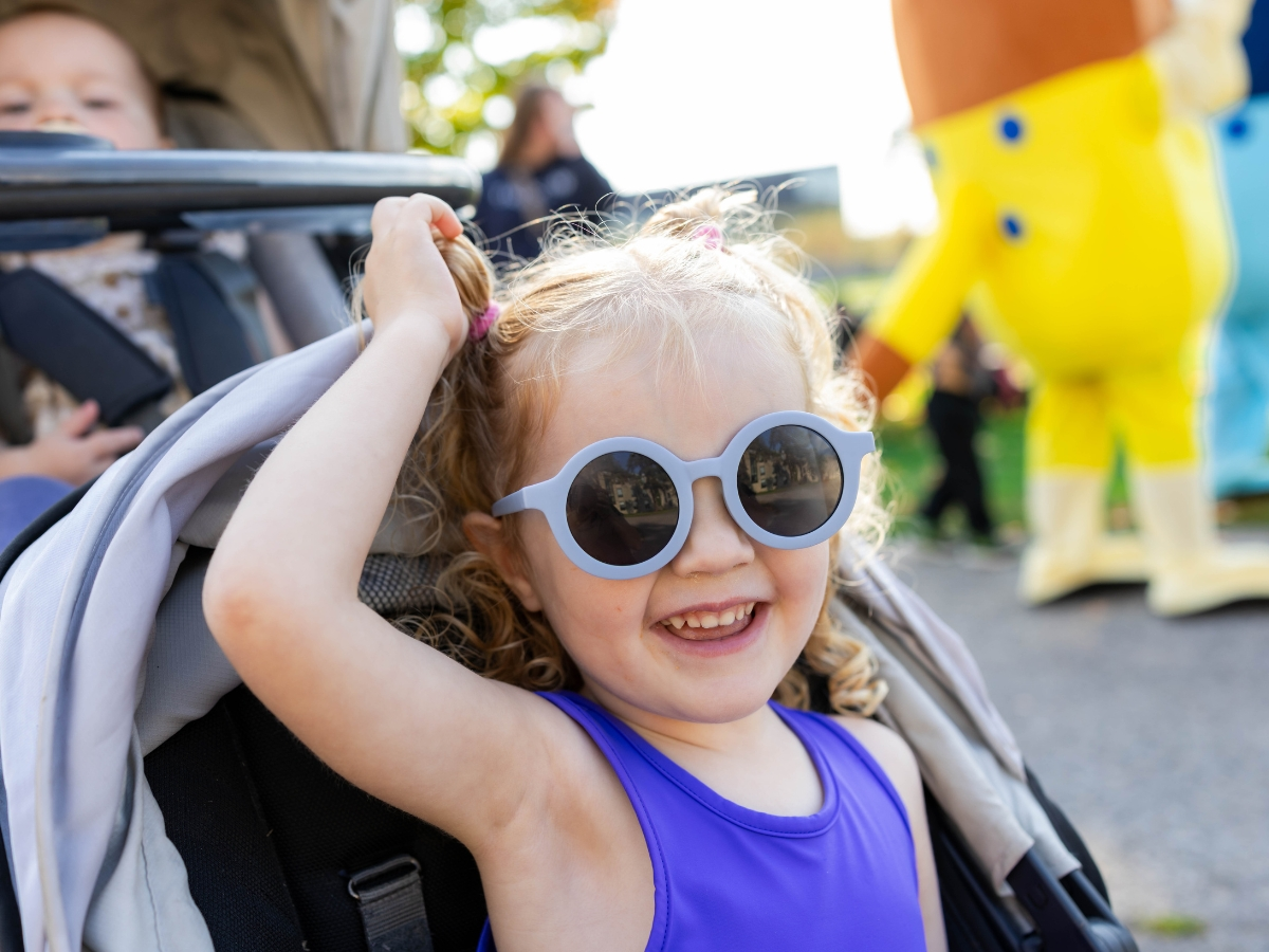 A child in a stroller, smiling at the camera with sunglasses on