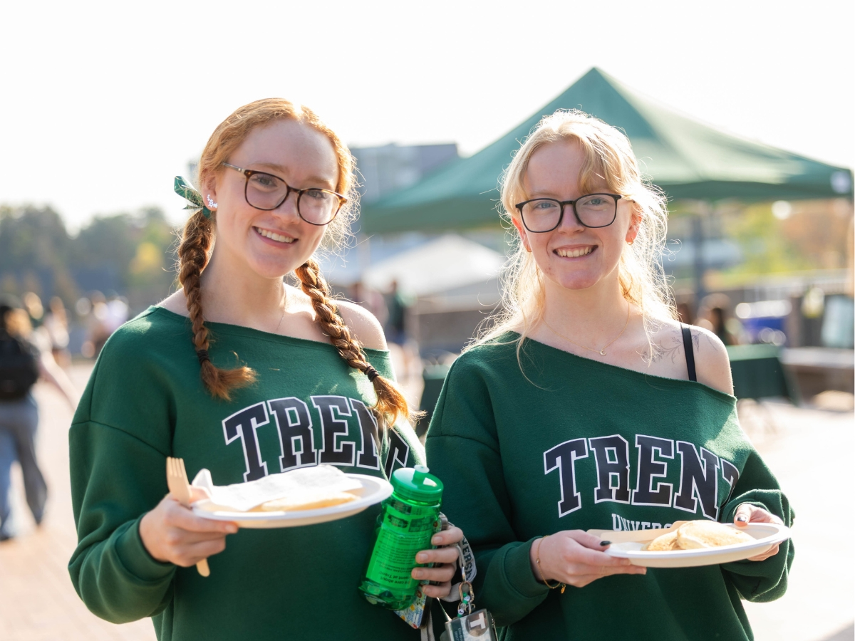 Two people smiling at the camera holding a plate of pancakes