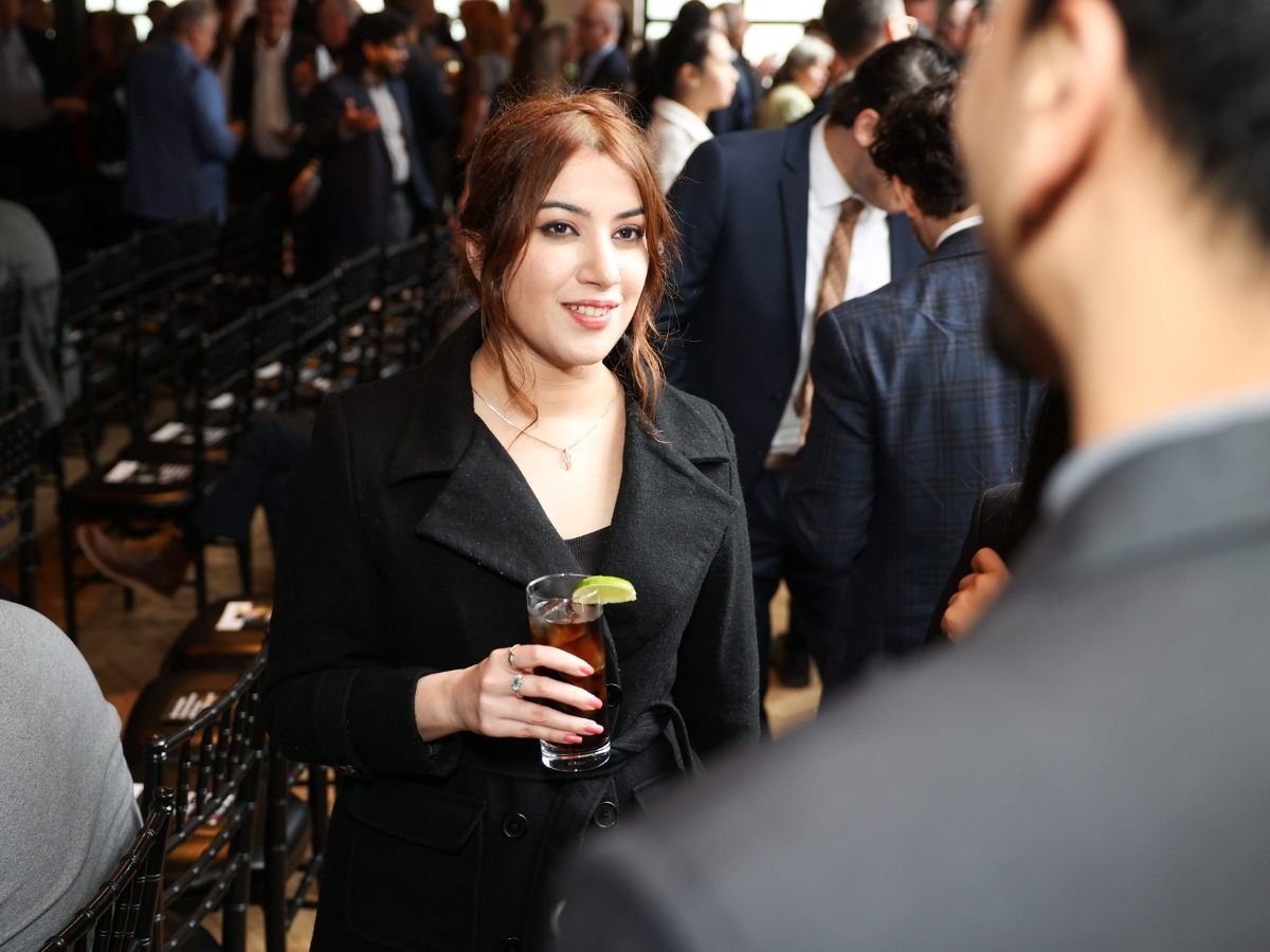 A woman smiling at someone behind the camera, holding an iced tea