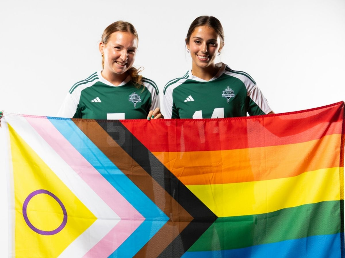 Two women soccer players holding Pride flag