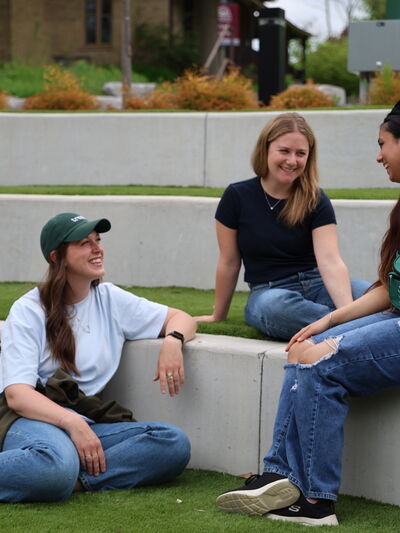 Three alumni sitting at Traill College ampitheatre