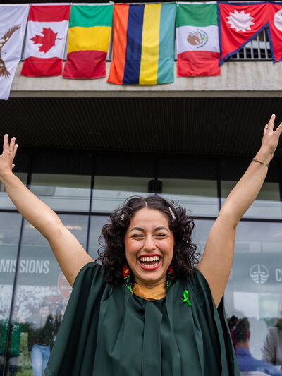 Women in graduation regalia smiling with her arms up