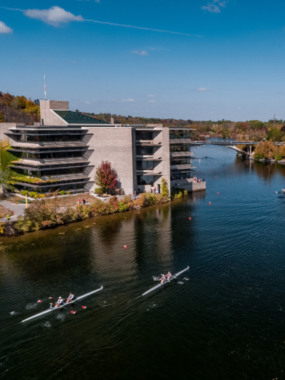 An aerial shot of the Otonabee River with Bata Library in the background. Two rowers are in the water.