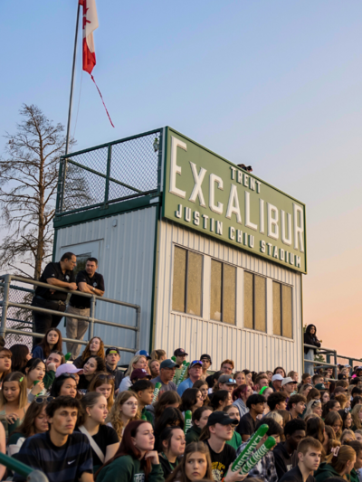 People in the stands of a outdoor game with an Excalibur sign and sunset in the background