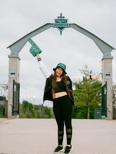 Women standing beneath Trent Excalibur arch with arms up, Trent foam finger and bucket hat on