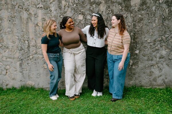 4 women standing against concrete wall smiling at each other