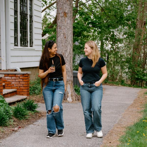 2 women talking and walking on paved path outside a house