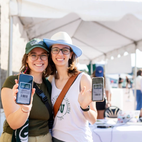 Two Trent alumni hold up their phones showing the Trent Alumni Perks app