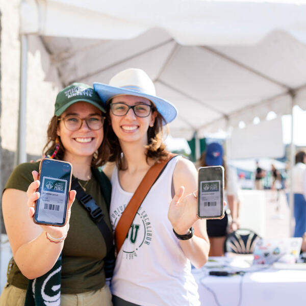 Two Trent alumni hold up their phones showing the Trent Alumni Perks app